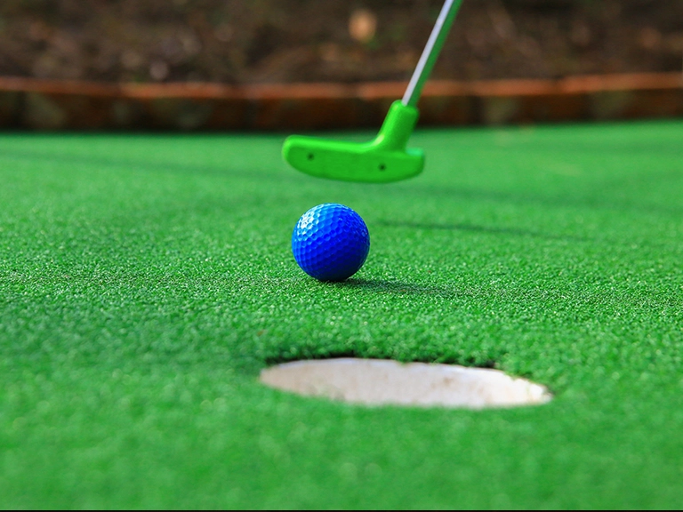 A blue mini golf ball dropping into the cup on a Steel City mobile mini golf hole